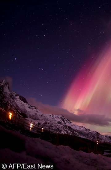 A surfer looks at the Northern lights ( aurora borealis ) illuminating the sky over the snow covered beach of Unstad, on Lofoten Islands, Arctic Circle