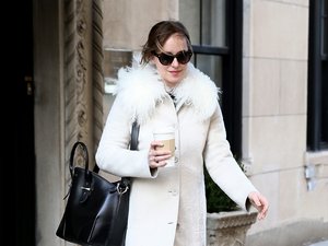 Dakota Johnson w białym płaszczu i czarnych spodniach z kubkiem