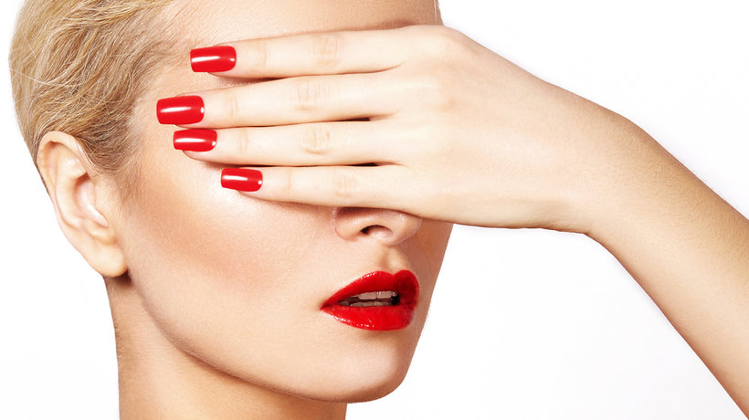 Kobieta w czerwonej szmince i z czerwonymi paznokciami zasłaniająca twarz dłonią
